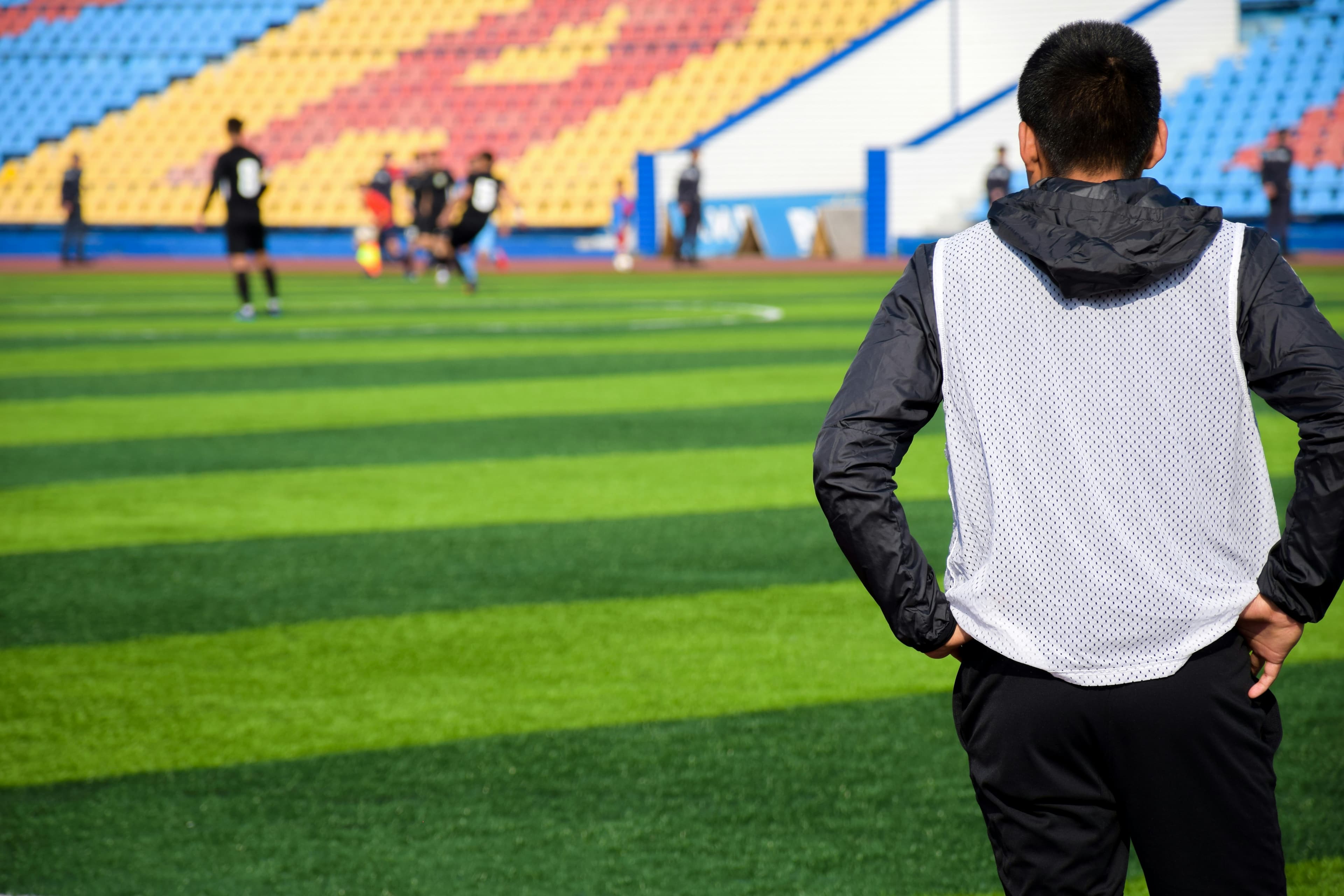 A coach watching a team train on a sunny sports field